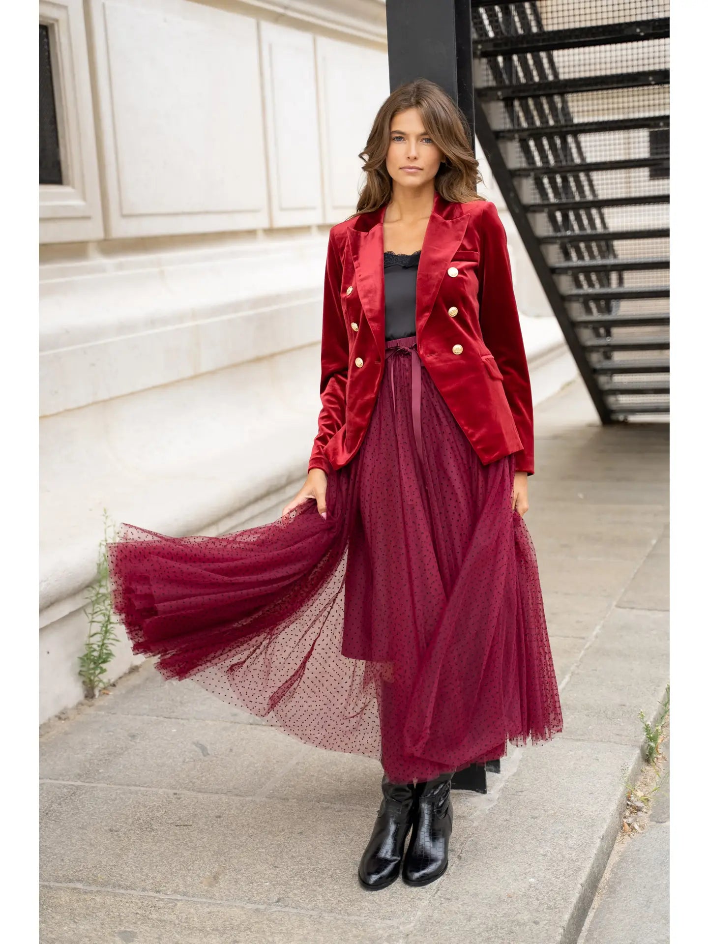 Woman wearing a red jacket and burgundy dress standing on a city street.