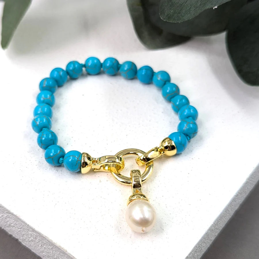 Turquoise beaded bracelet with a gold clasp and pearl charm on a white background