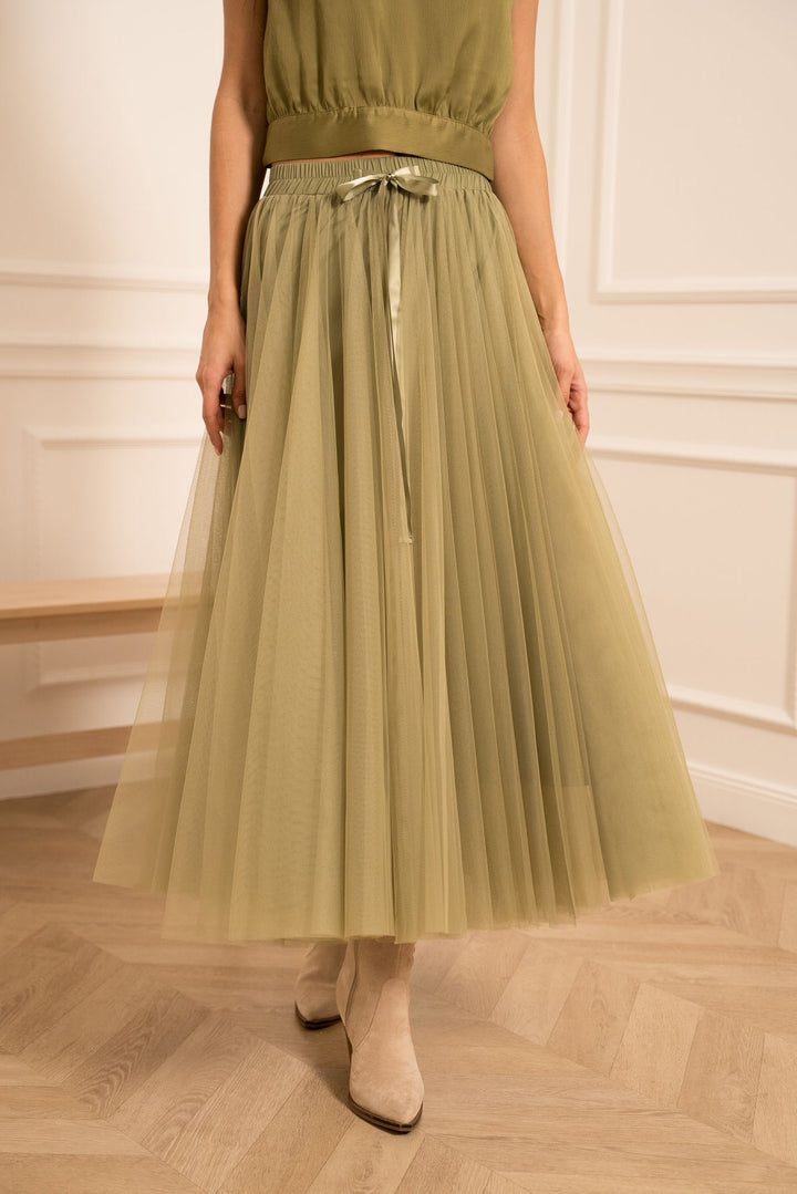 Person wearing a green pleated skirt with a plain background