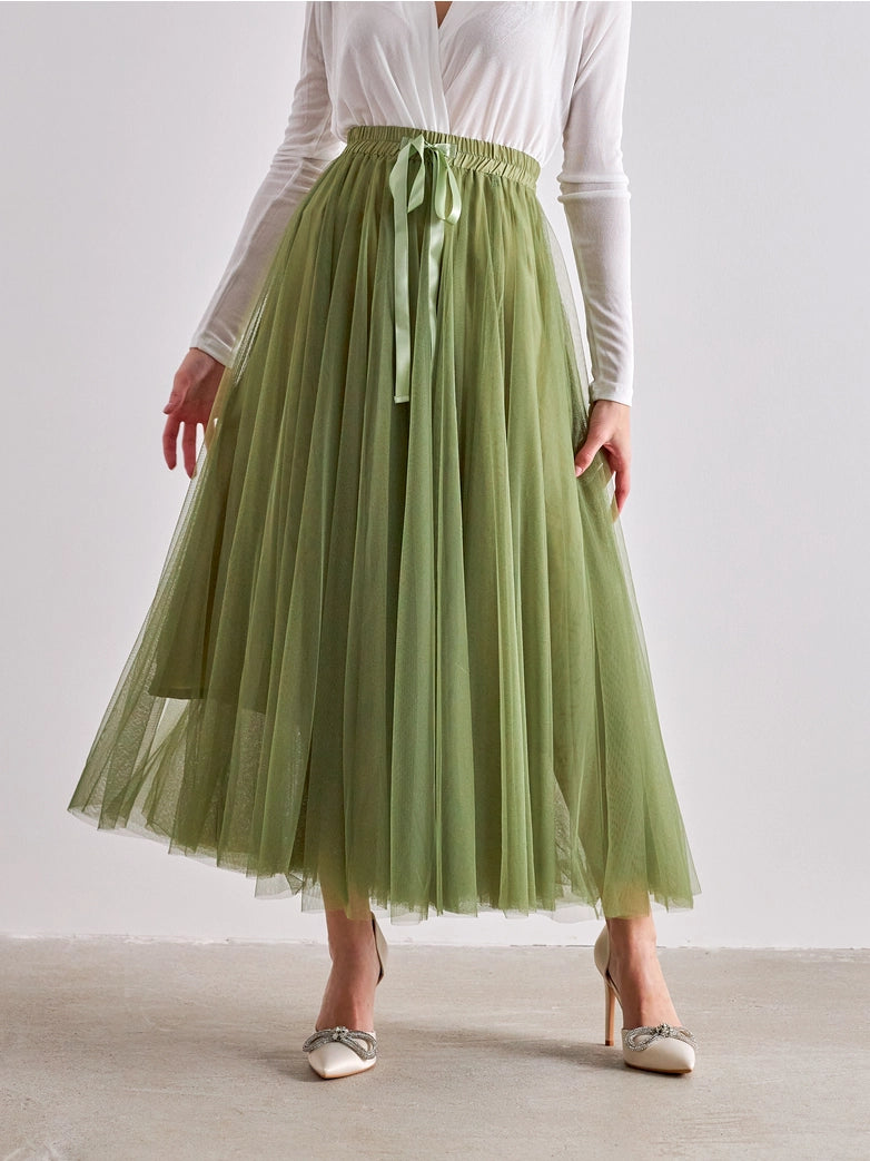 Person wearing a green tulle skirt with a white top on a plain background