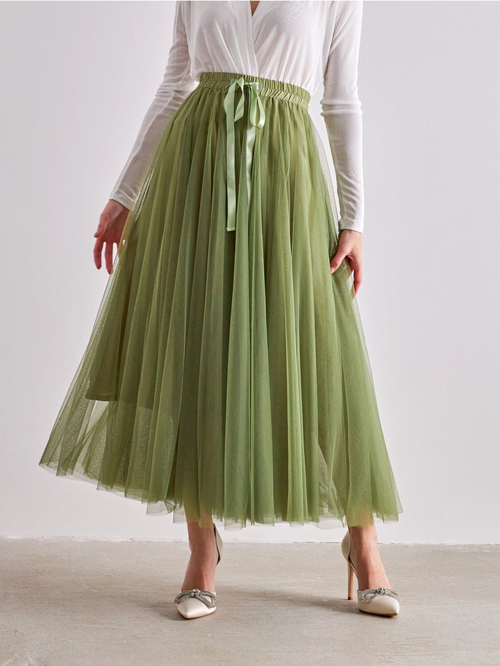 Person wearing a green tulle skirt with a white top on a plain background
