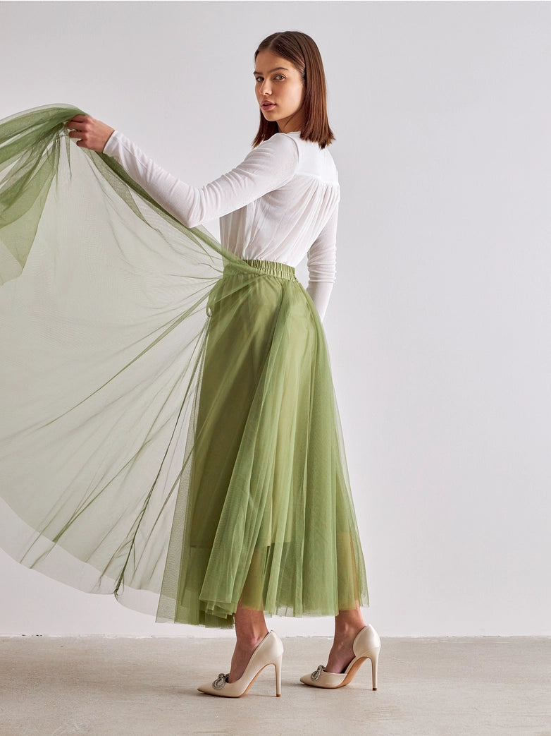 Woman wearing a white top and green skirt against a plain background