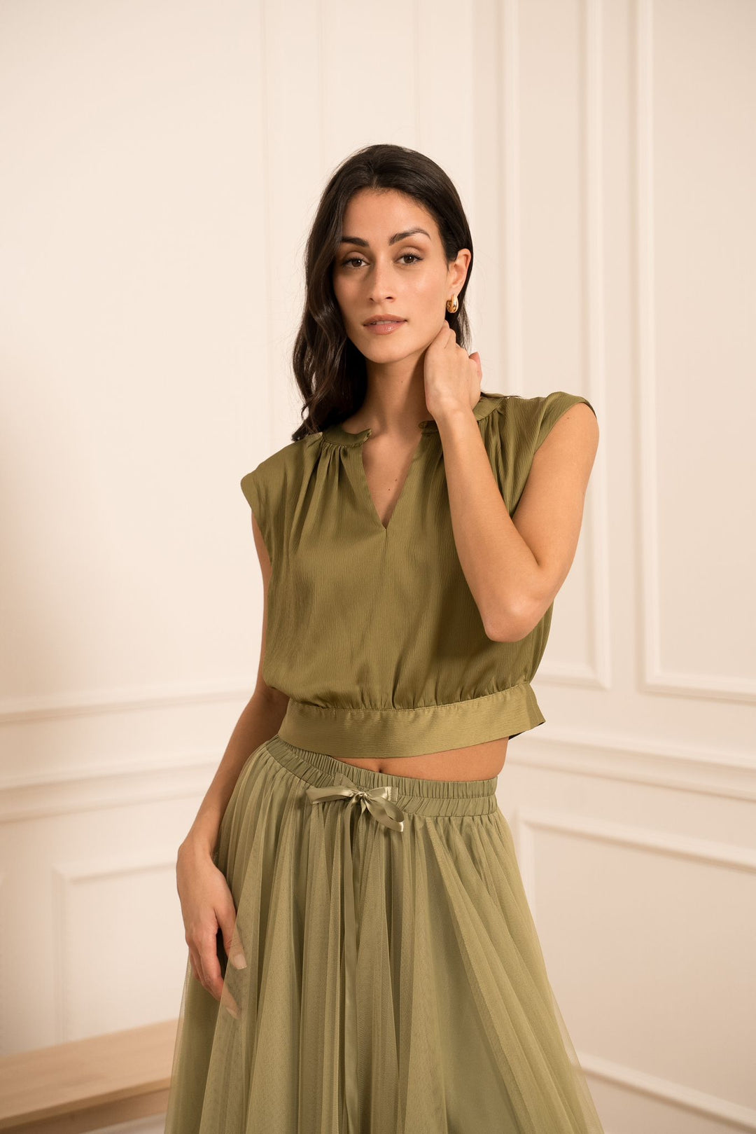 Woman wearing an olive green outfit against a white wall