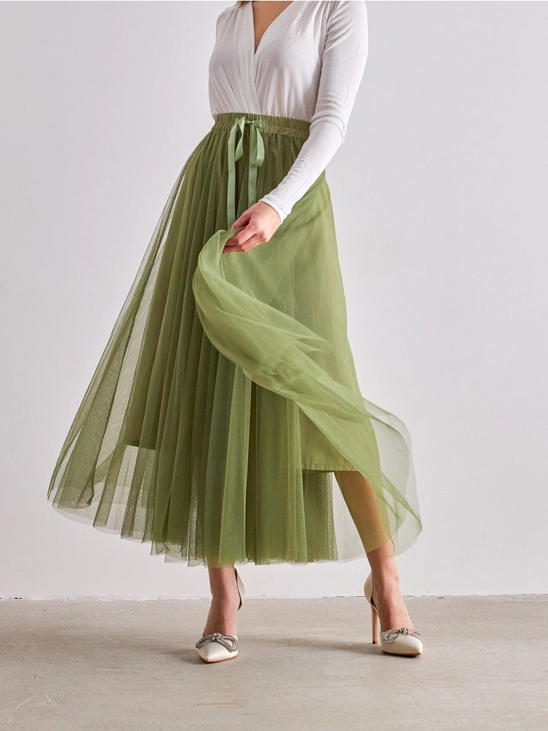 Person wearing a white top and green pleated skirt on a plain background