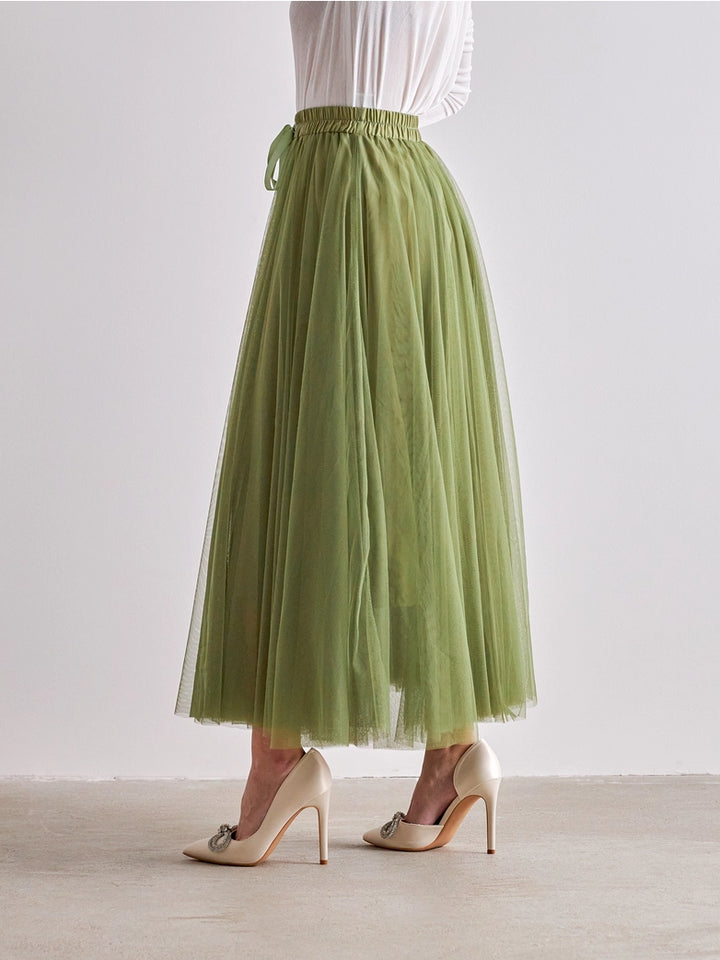 Person wearing a green tulle skirt and white high-heeled shoes on a plain background