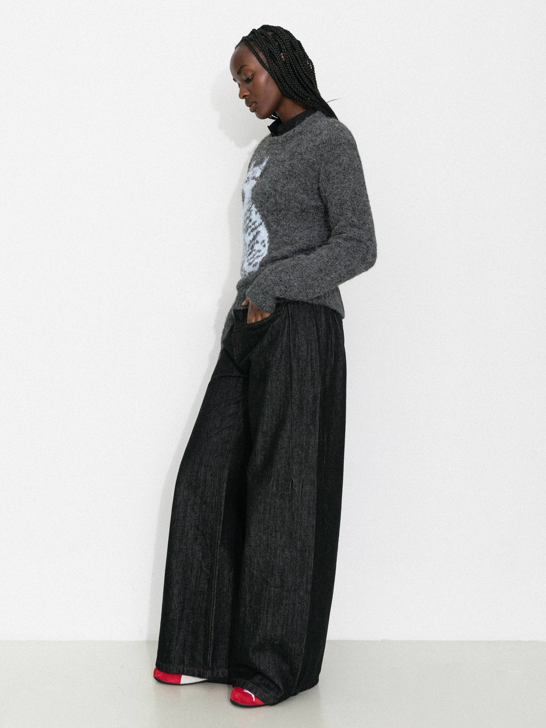 Person wearing a gray sweater and black wide-leg pants against a white background