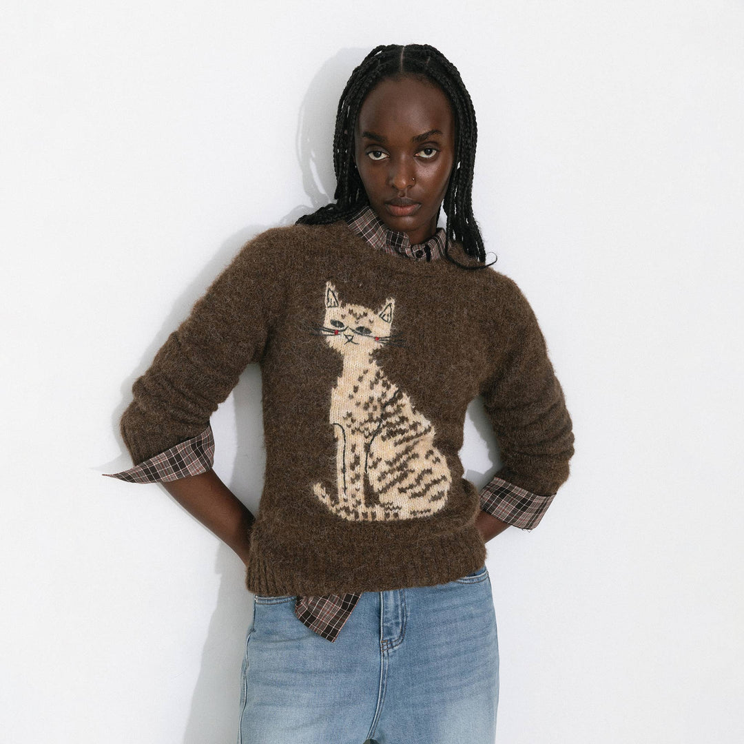 Person wearing a brown sweater with a cat design on a white background