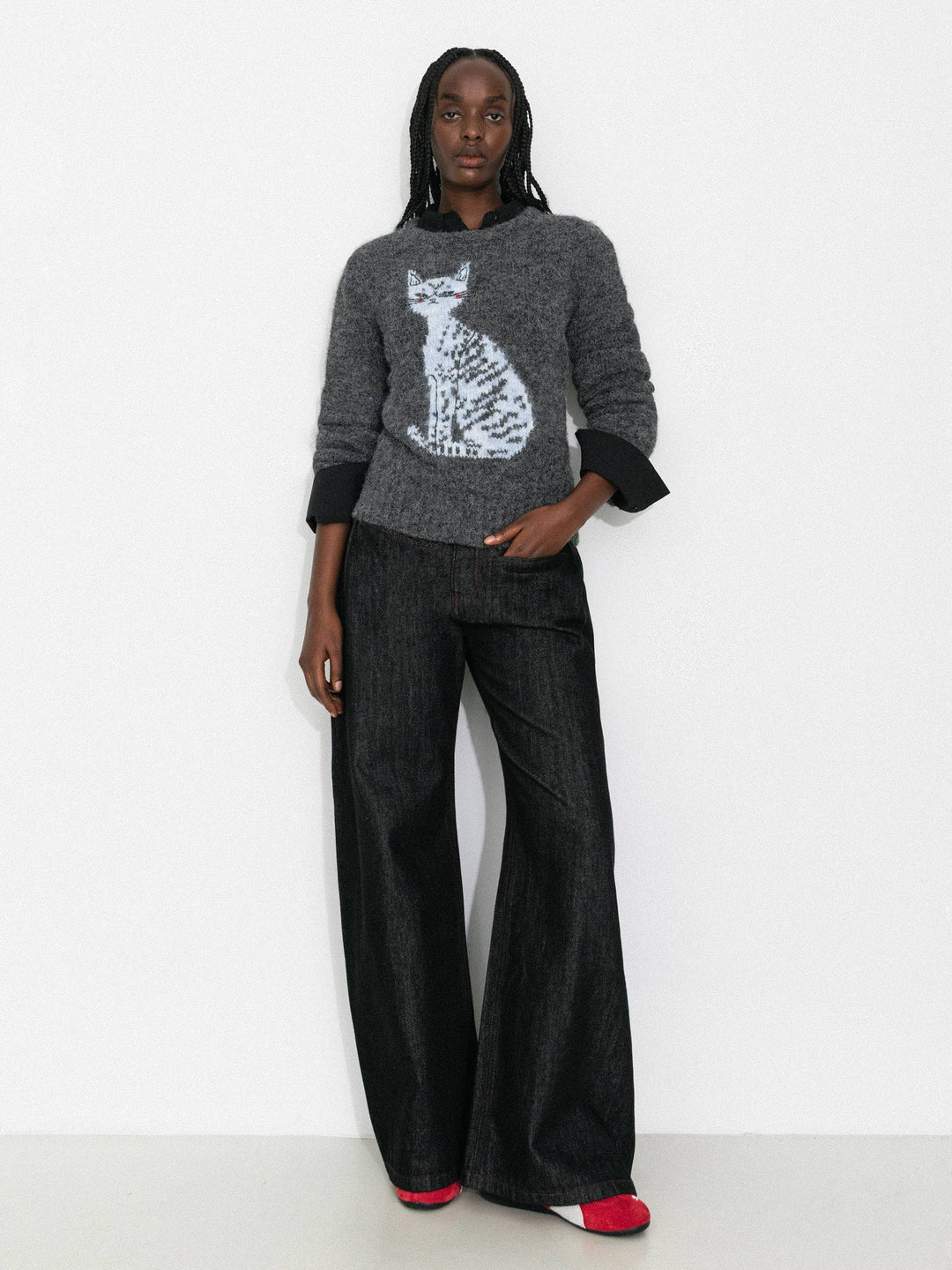 Person wearing a gray sweater with a cat design and black pants on a white background