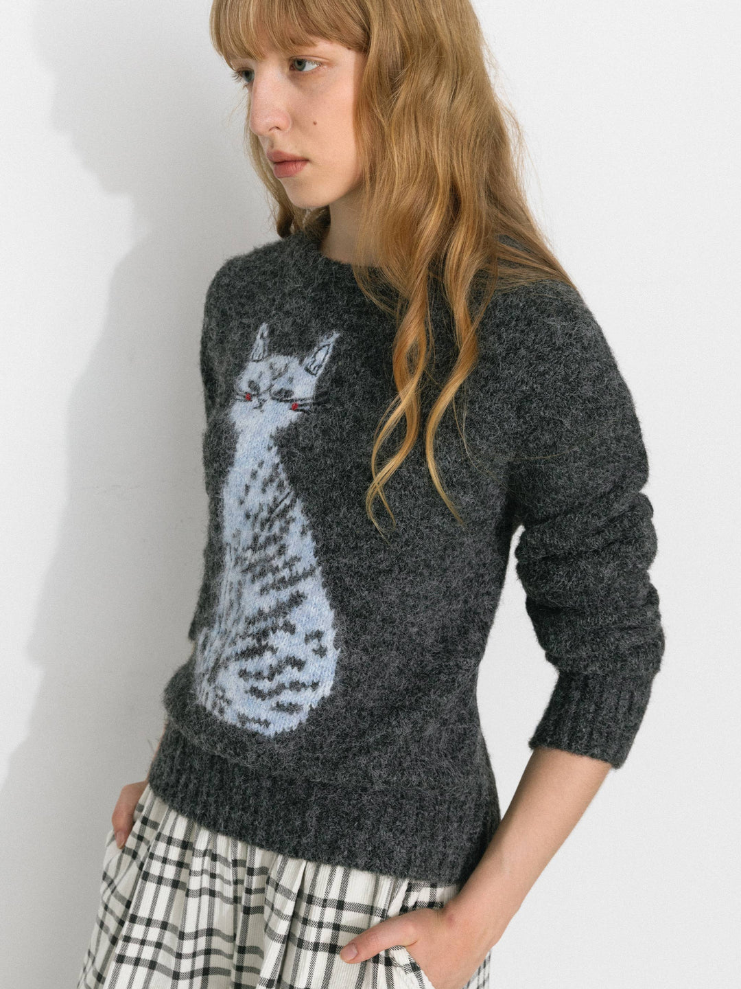 Person wearing a dark gray sweater with a cat design on a white background