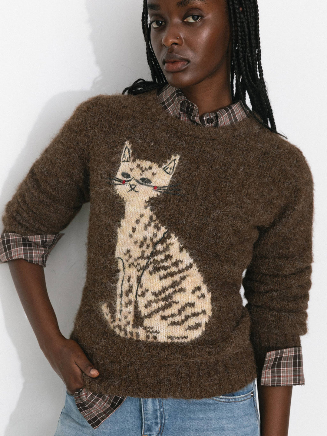 Person wearing a brown sweater with a cat design on a plain background