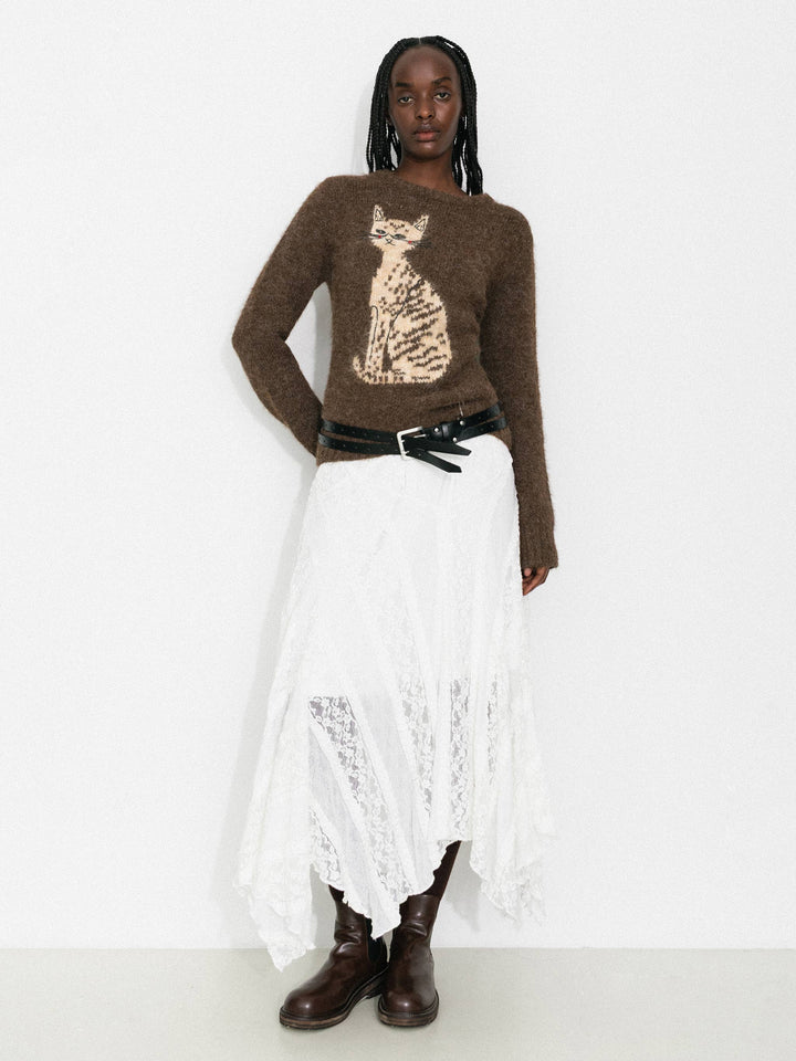 Person wearing a brown sweater with a cat design, white skirt, and brown boots on a white background