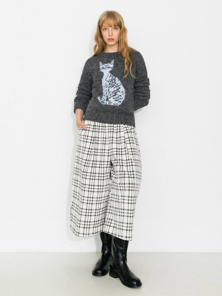 Woman wearing a gray sweater with a cat design and plaid pants on a white background