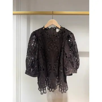 A black lace short-sleeve blouse hanging on a wooden hanger against a light gray wall with a gold clothing rack bar visible at the top.