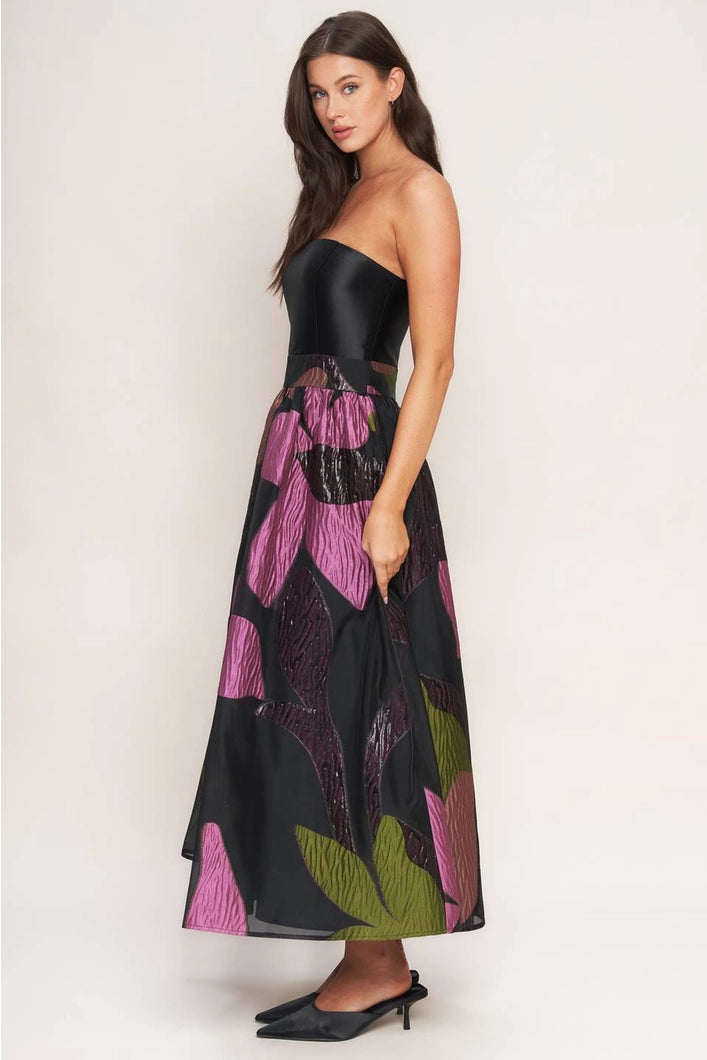 Woman wearing a strapless black dress with pink and green floral patterns on a white background