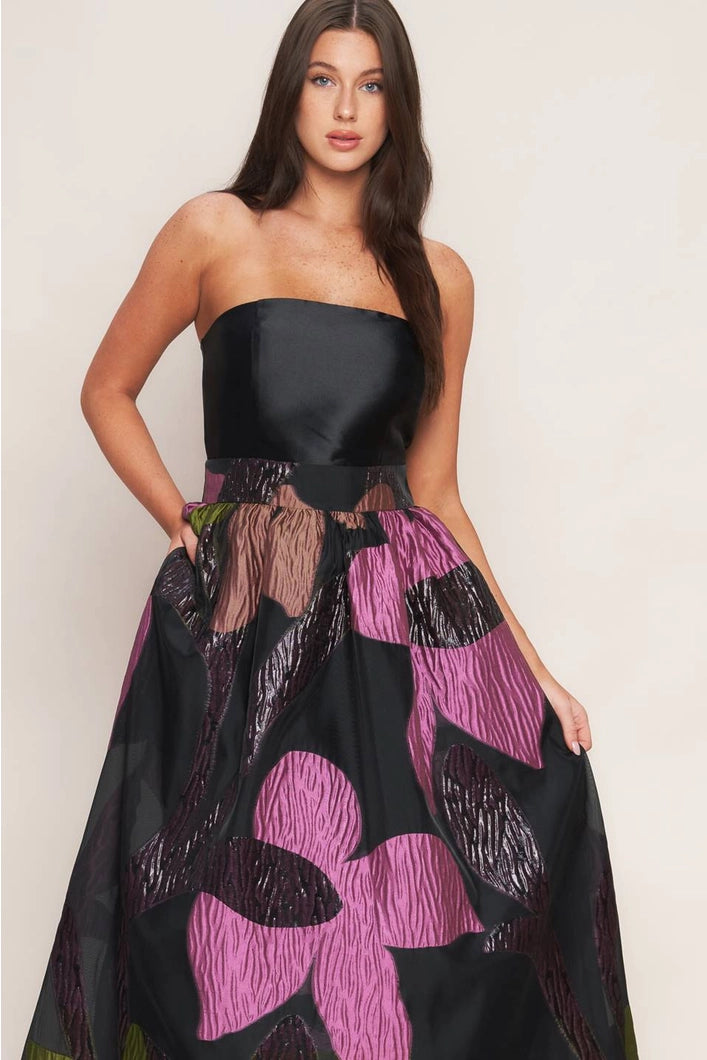 Woman wearing a strapless black dress with a colorful floral pattern on a plain background