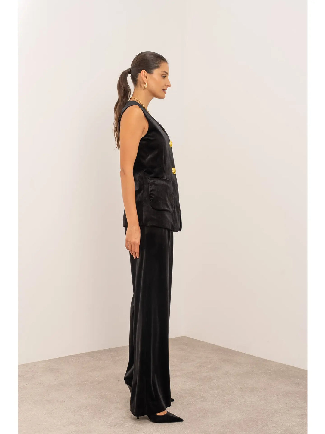 Woman wearing a black sleeveless top and pants against a white wall.