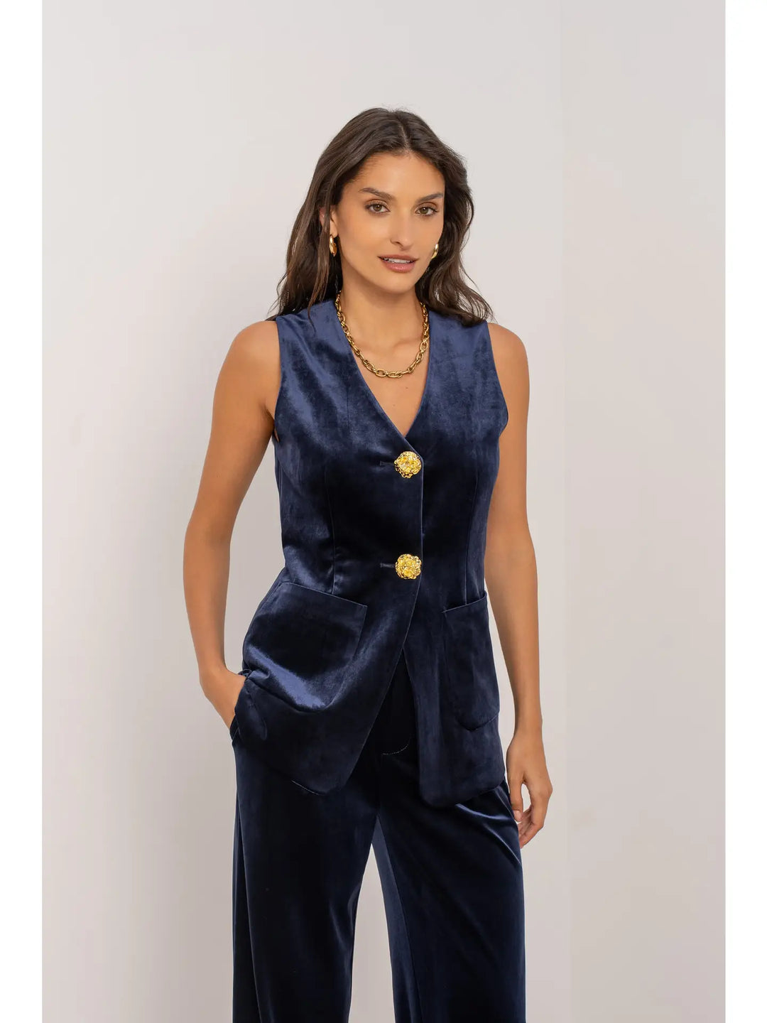 Woman wearing a navy blue vest with gold buttons on a plain background