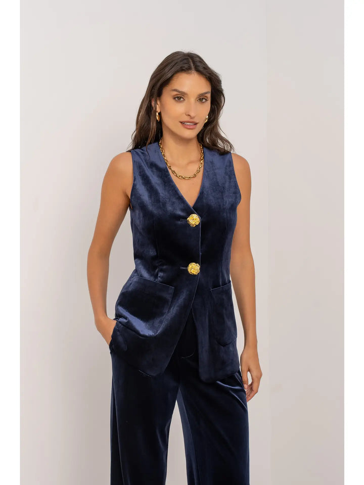 Woman wearing a navy blue vest with gold buttons on a plain background