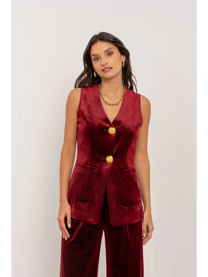 Woman wearing a burgundy sleeveless top with gold buttons and matching pants on a white background