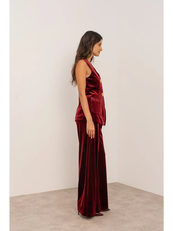 Woman wearing a burgundy velvet jumpsuit against a white background