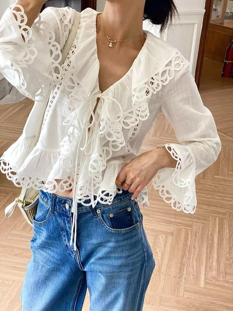 Person wearing a white lace blouse and blue jeans indoors.