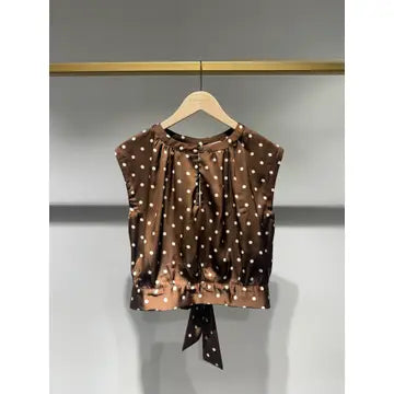 A brown sleeveless top with white polka dots, hanging on a wooden hanger against a gray wall.