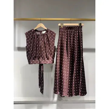 A two-piece women's outfit consisting of a sleeveless top and a matching midi skirt, both in a dark brownish-purple color with a white polka dot pattern. The top features a gathered, pleated bodice and a tie detail at the waist, while the skirt has an elastic waistband.