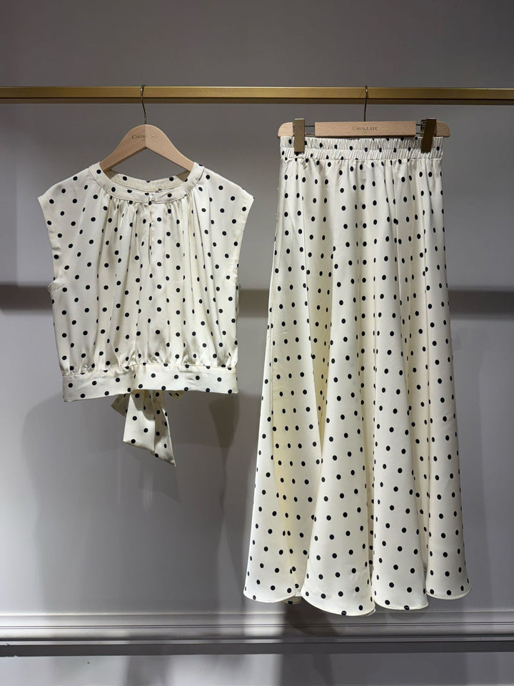 White outfit with black polka dots on hangers against a gray background