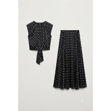 A two-piece women's outfit set featuring a sleeveless black crop top with a tie-front detail and a matching high-waisted pleated midi skirt, both decorated with a small white polka dot pattern, displayed on a light gray background.