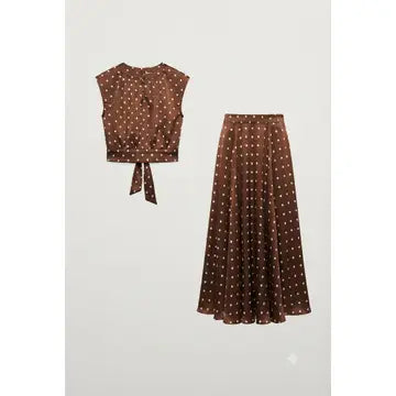 A two-piece women's outfit set featuring a sleeveless brown crop top with a tie-front waist and a matching pleated midi skirt, both decorated with a small white polka dot pattern, shown against a light gray background.