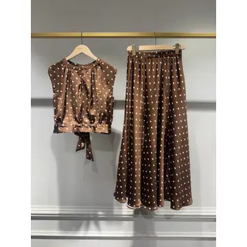 A two-piece women's outfit hanging on a clothing rack, featuring a brown short-sleeve crop top and matching high-waisted maxi skirt with a white polka dot pattern.