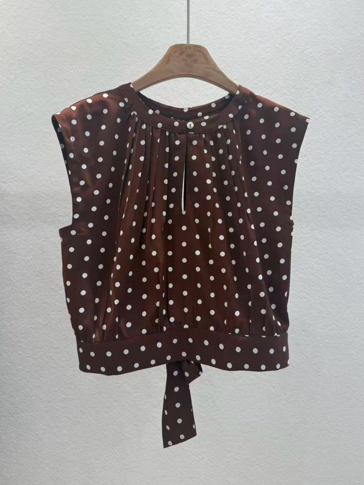Brown sleeveless top with white polka dots on a hanger against a light gray background
