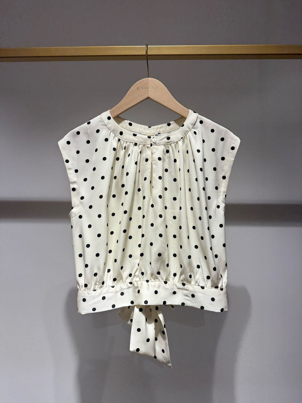 White blouse with black polka dots on a hanger against a gray background