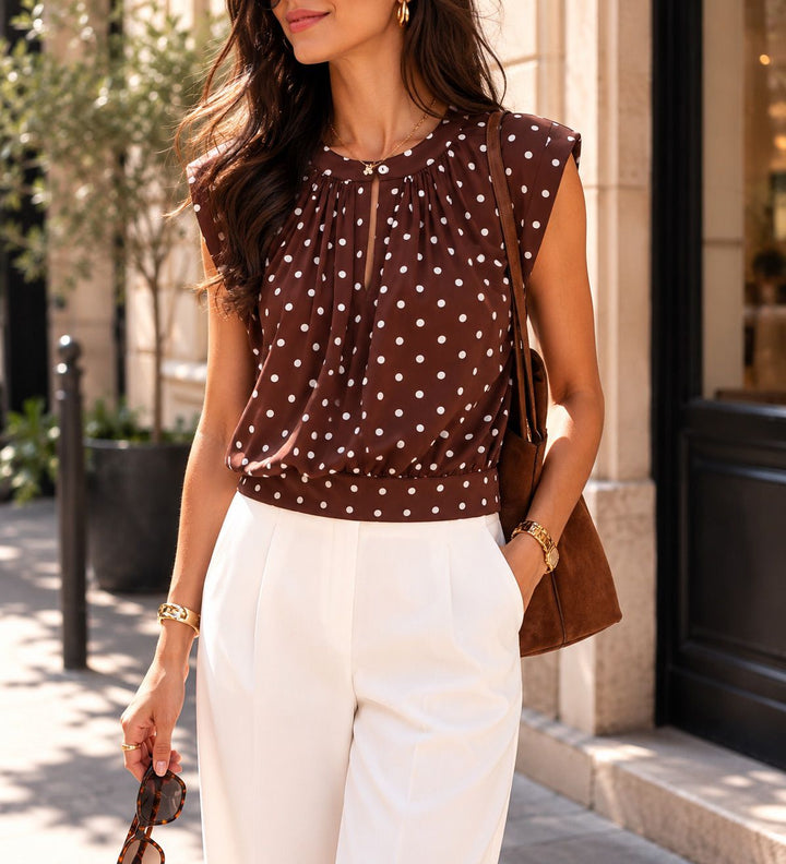 Woman wearing a brown polka dot top and white pants on a city street.