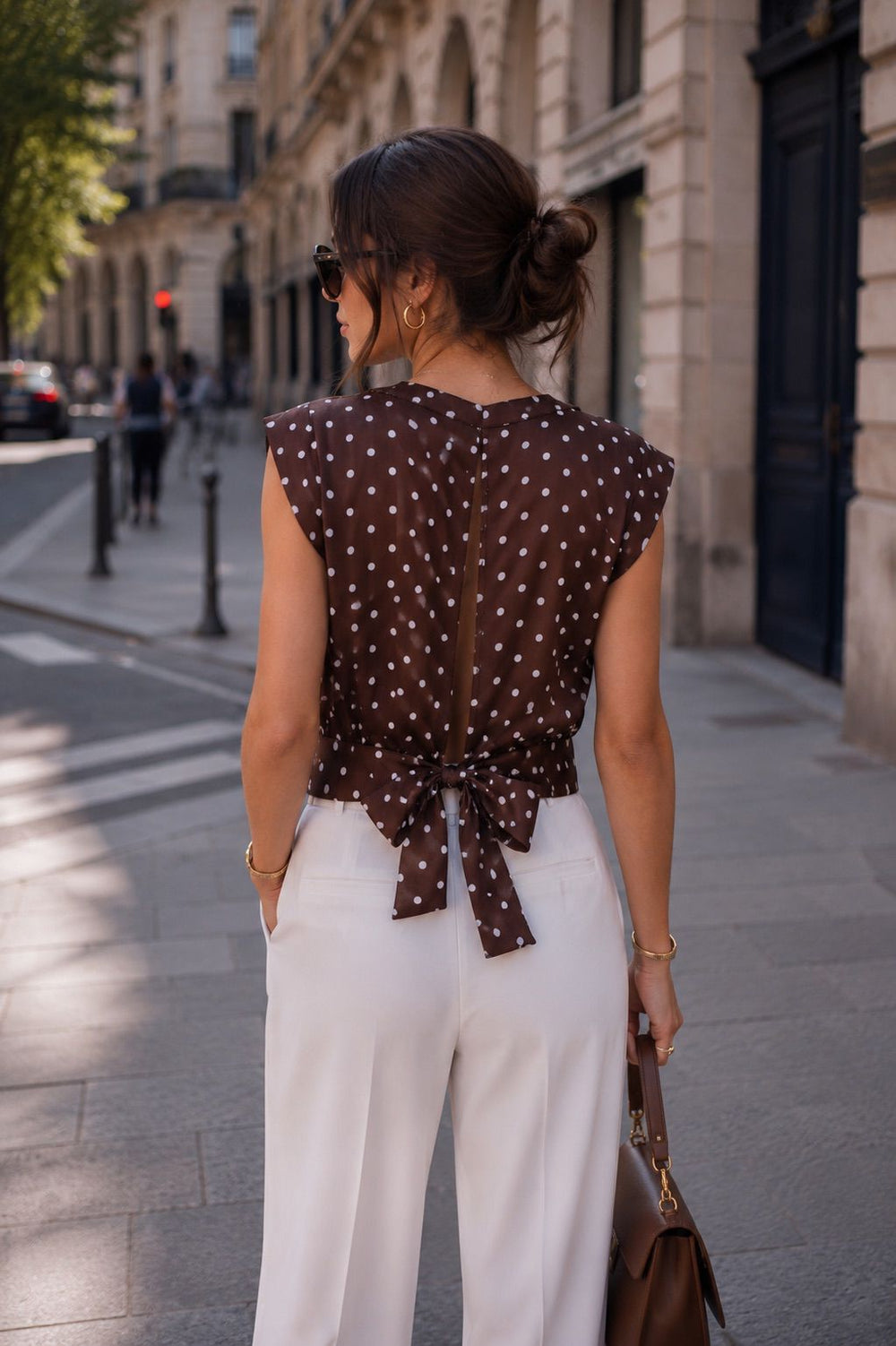 Woman in a polka dot top and white pants walking down a city street.