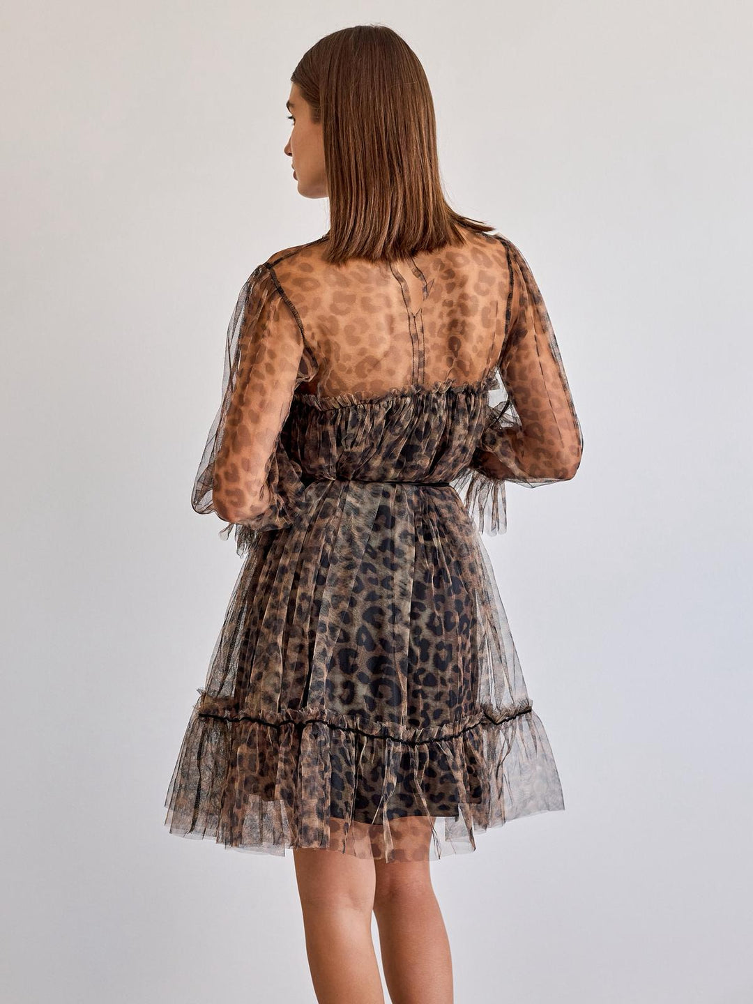Woman wearing a leopard print dress with sheer sleeves on a plain background