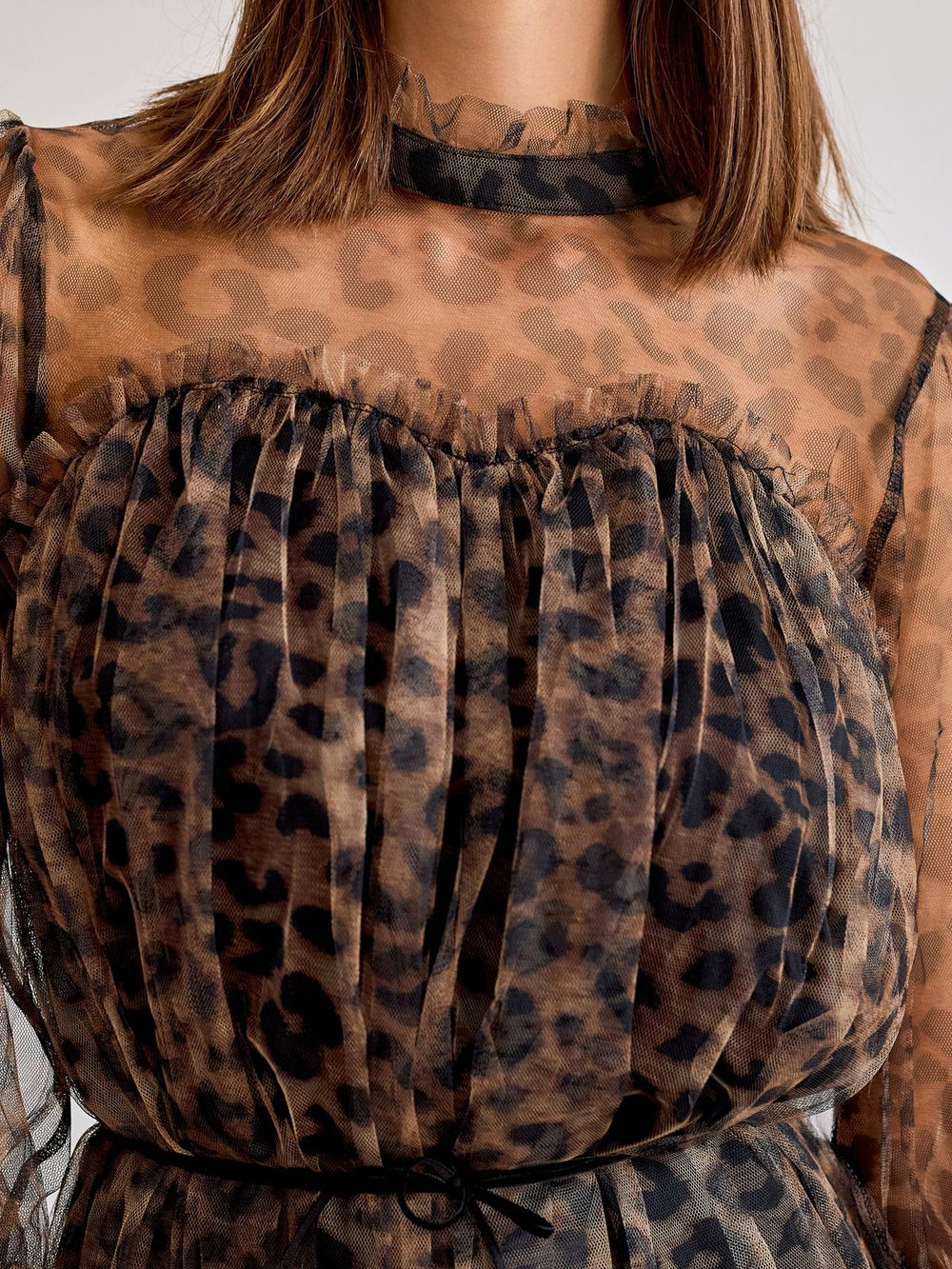 Leopard print sheer top with ruffled details on a neutral background