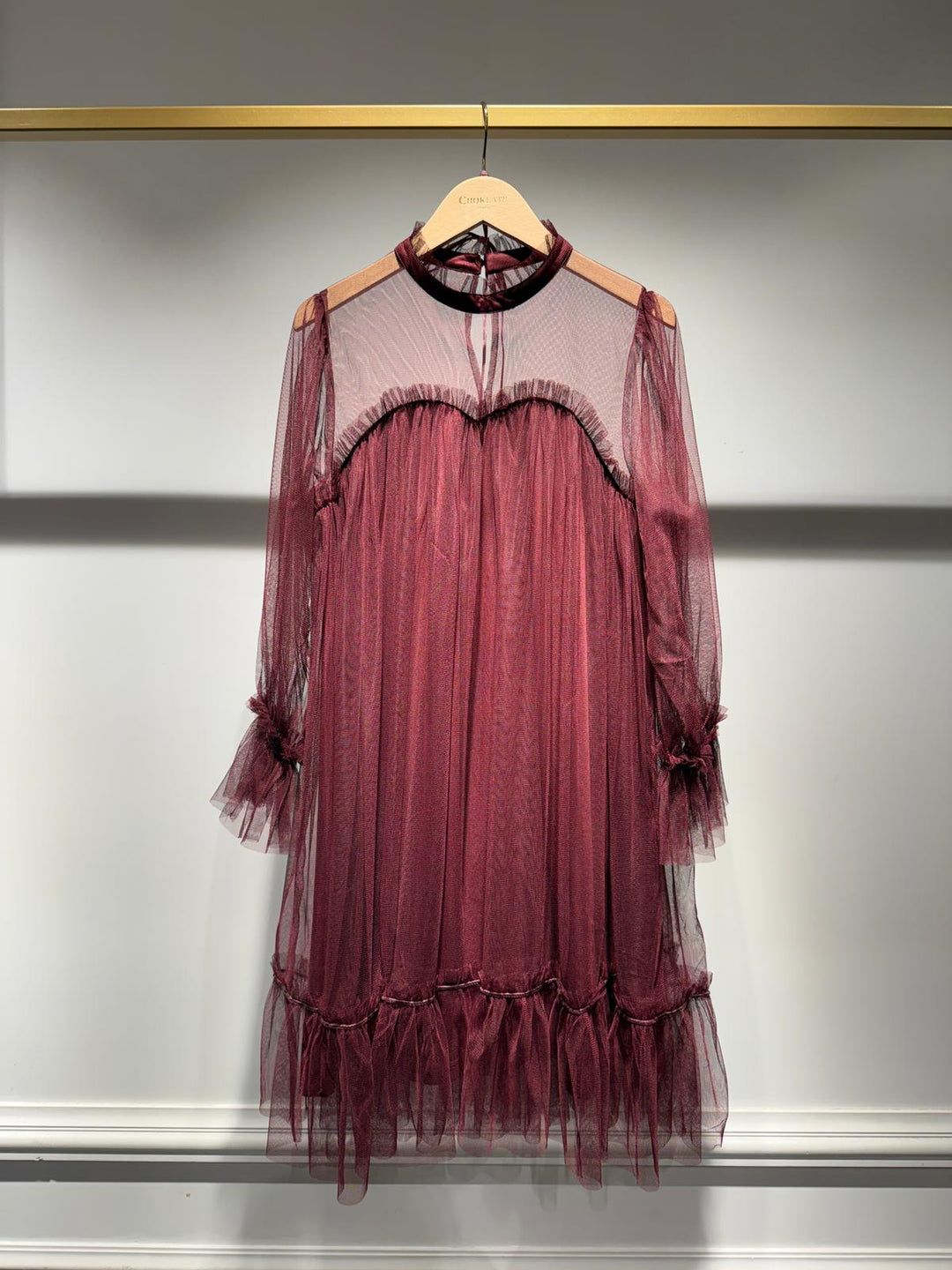 Maroon tulle dress on a hanger against a neutral background