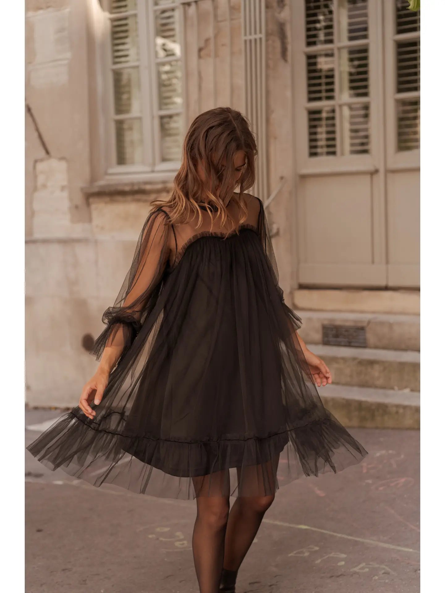 Woman wearing a black dress with sheer overlay walking on a street.