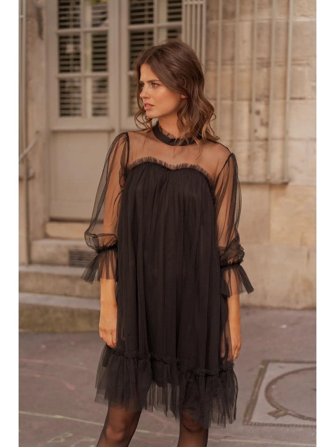 Woman wearing a black dress with sheer sleeves in an urban setting