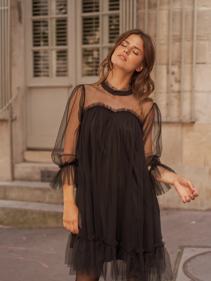 Woman wearing a black dress with sheer sleeves and neckline, standing outdoors.