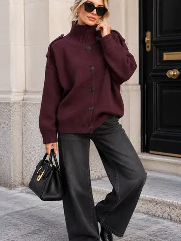 A woman wearing a burgundy turtleneck cardigan sweater, black wide-leg jeans, black sunglasses, and carrying a black handbag, posing outdoors in front of a building with a black door.