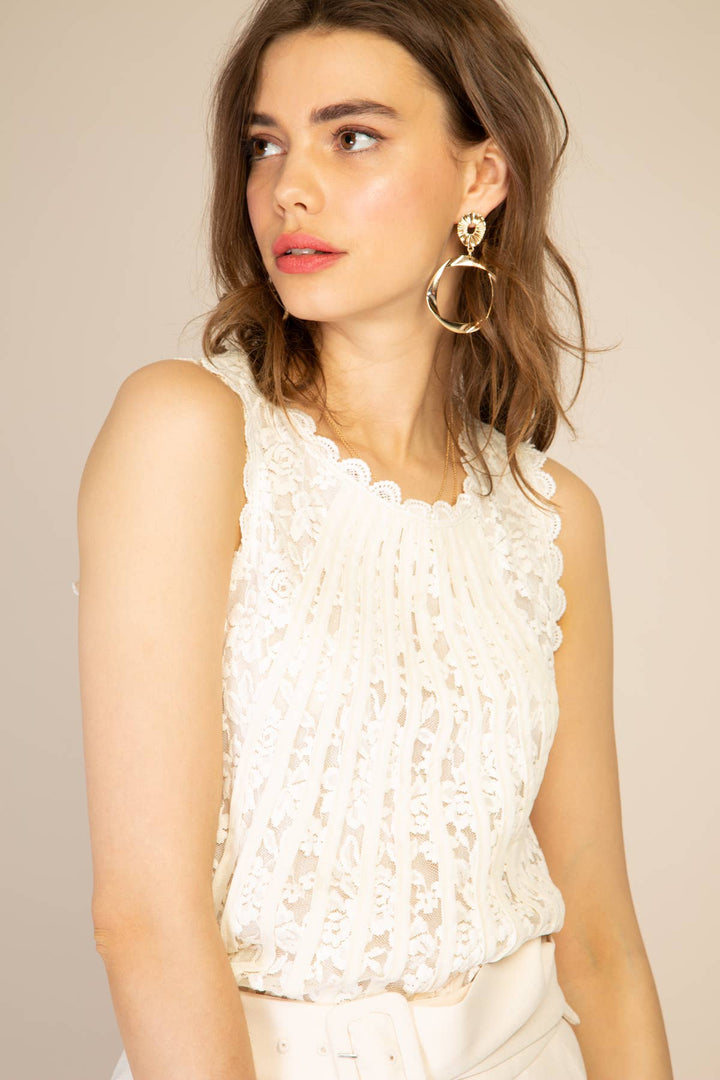 Woman wearing a white sleeveless top with ruffled details against a beige background