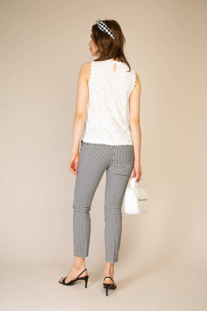 Woman wearing a white sleeveless top and black and white checkered pants on a beige background
