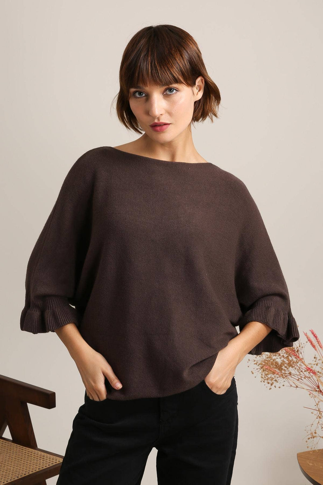 Woman wearing a brown sweater and black pants against a plain background