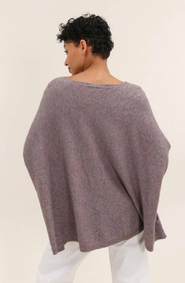 Person wearing a loose-fitting, light purple sweater over a white outfit on a plain background