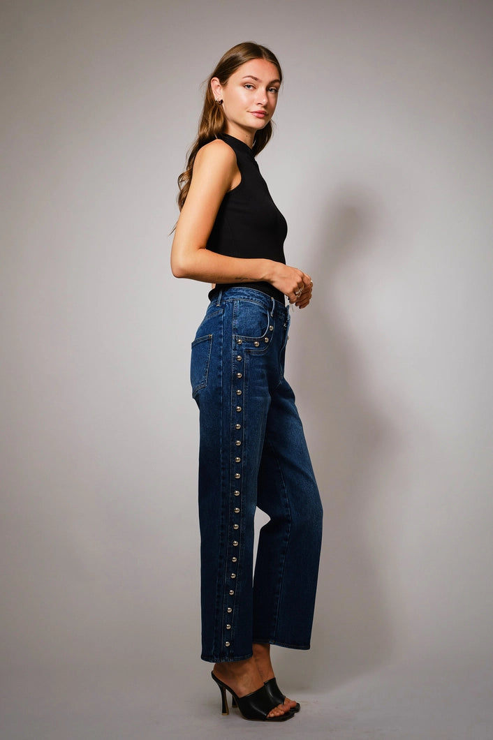 Woman wearing blue jeans with button details against a plain background