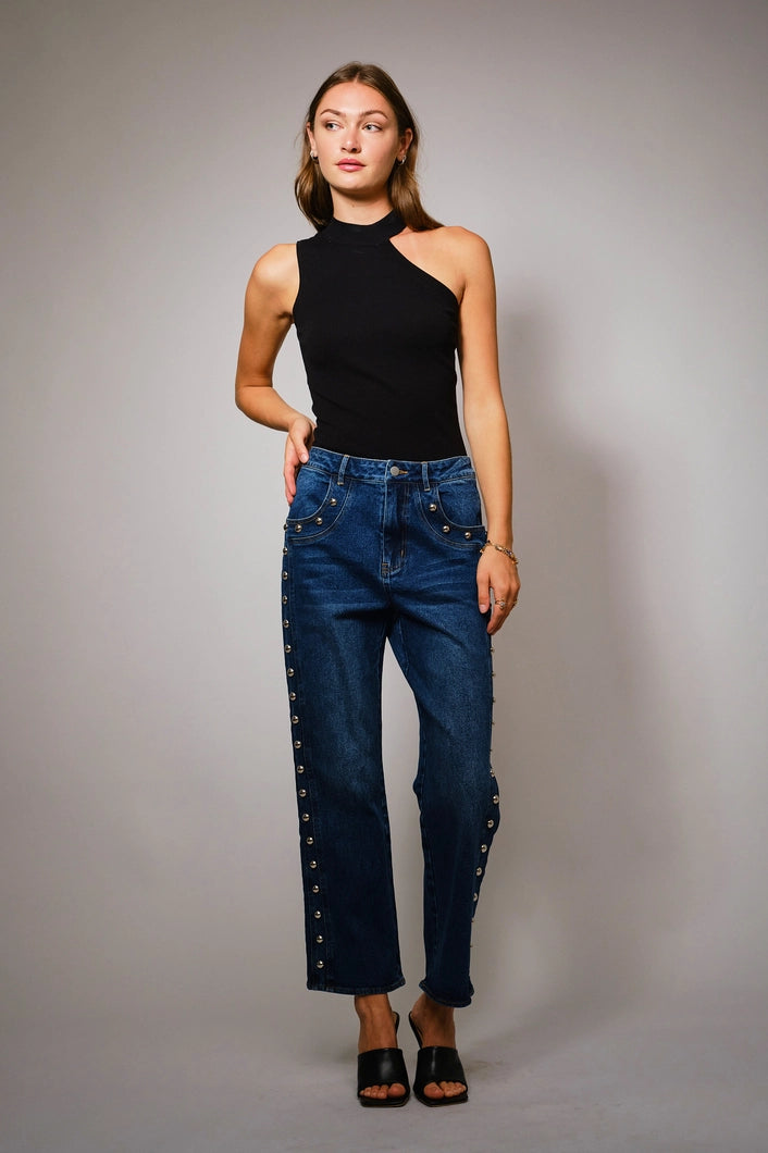 Woman wearing a black sleeveless top and blue jeans with studded details on a gray background