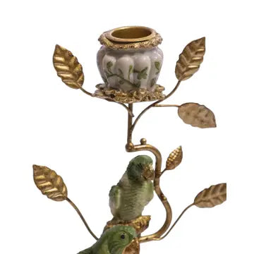 An ornate metal and ceramic candlestick holder featuring a small green bird figurine perched on a gold-toned branch with leaf-shaped arms and a floral ceramic cup.