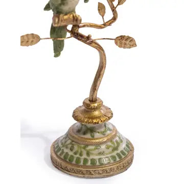An ornate vintage-style metal and ceramic candle holder featuring a gold-tone branch with leaf-shaped candle arms, a green bird figurine perched on top, and a decorated ceramic base.